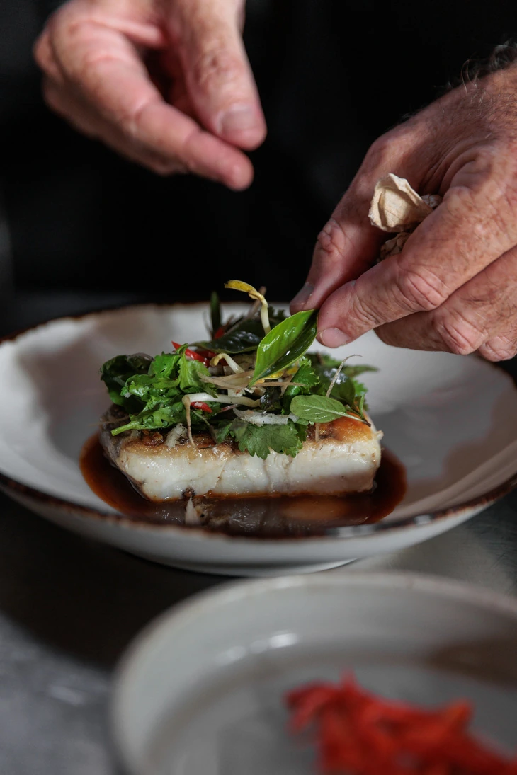 A chef finishing a fillet of fish with herbs at the pass at Seed