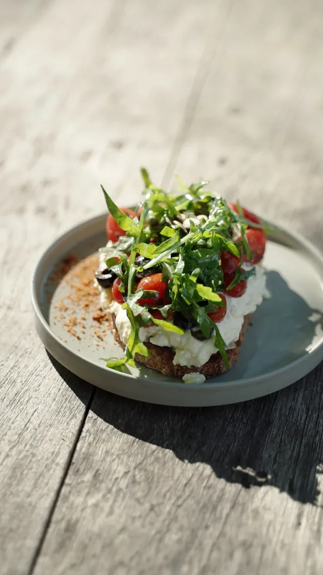 Whipped ricotta bruschetta with tomatoes, olives and shredded basil on a sunlit table at Seed