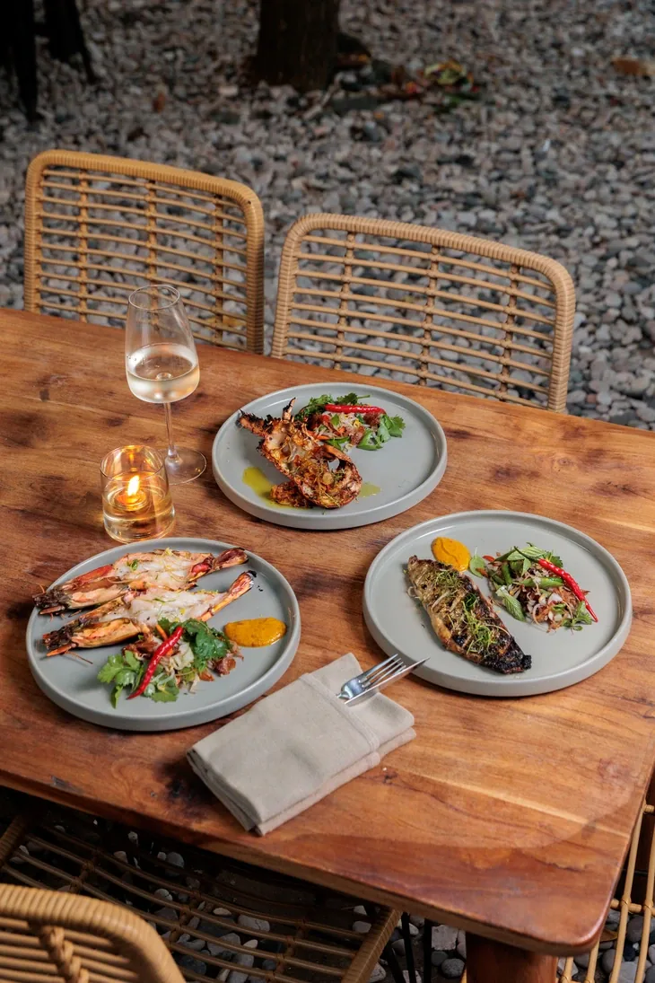 Grilled prawns, whole fish and salad laid across a garden table at Seed with a glass of white wine