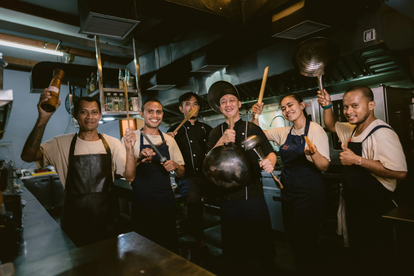 The Seed kitchen team posing with pans and wooden spoons raised in the kitchen in Bingin