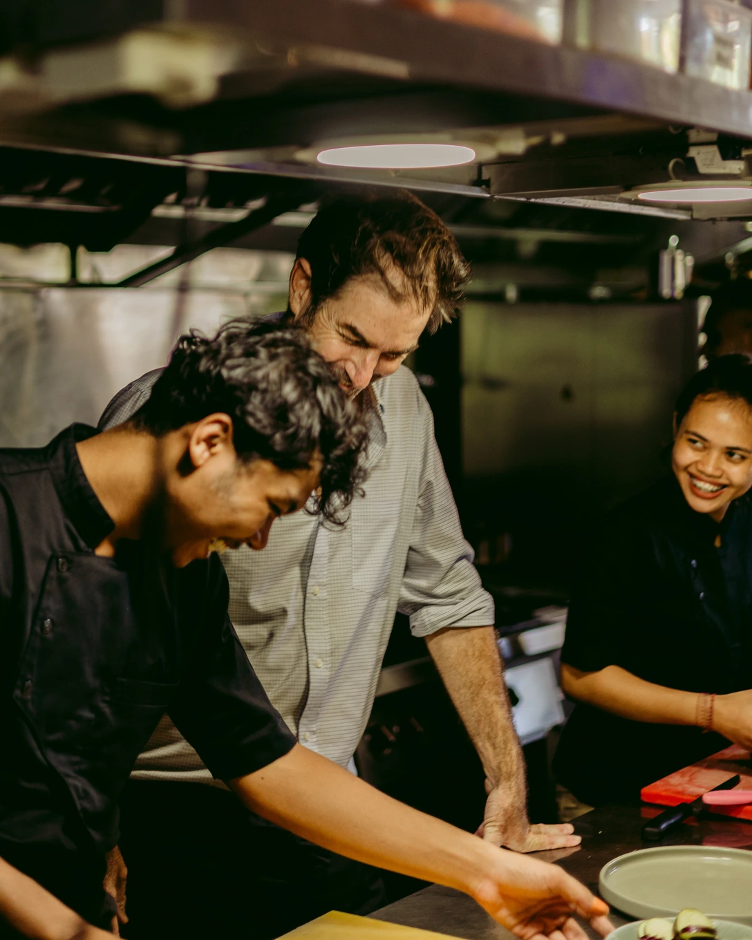 Chefs working and laughing together at the pass in the Seed kitchen in Bingin