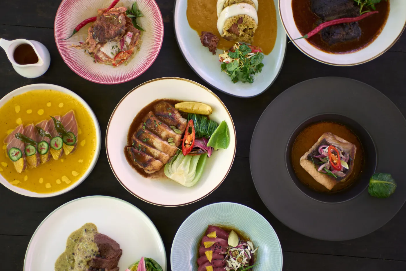 An overhead spread of Seed dishes on a dark table, from carpaccio to duck and grilled fish